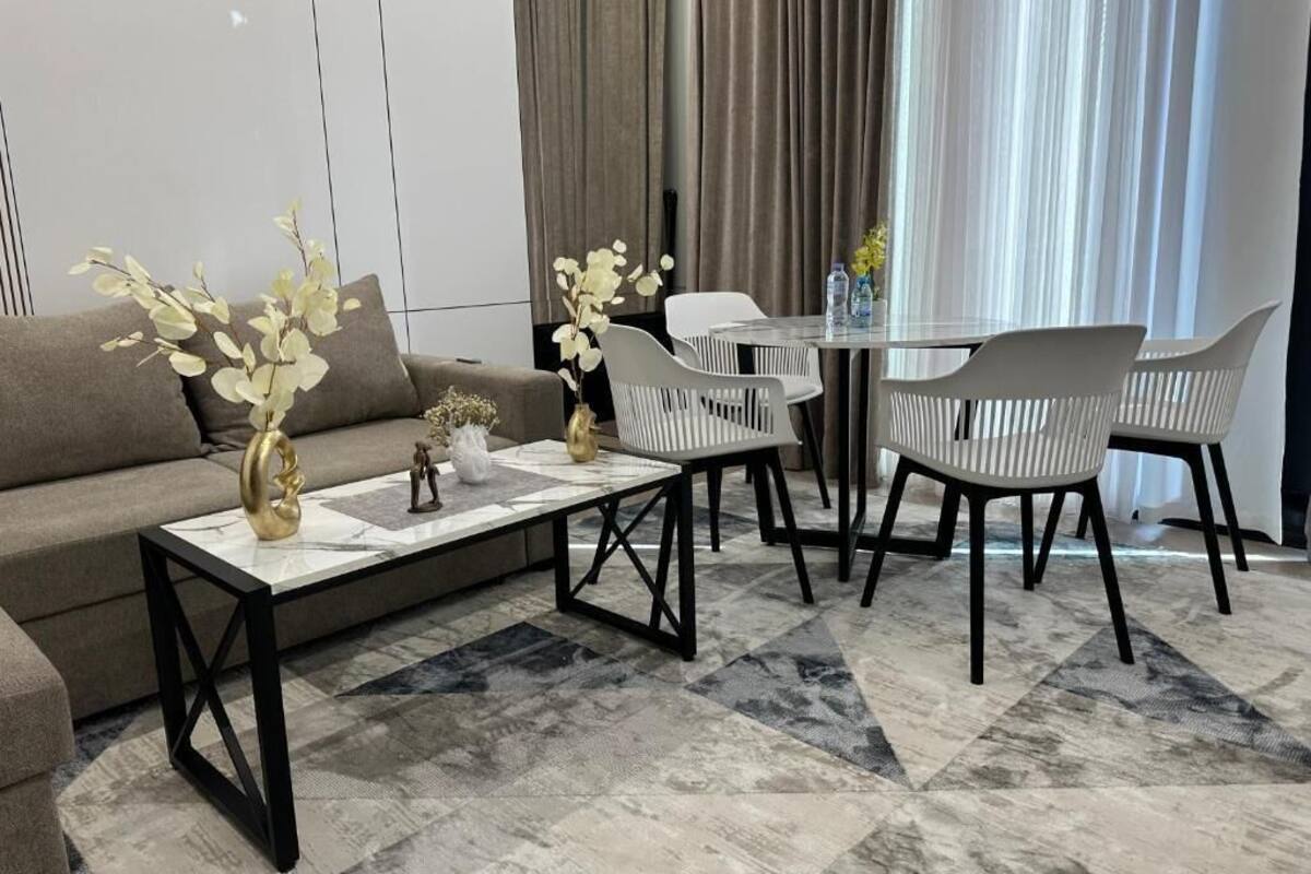 Una sala moderna con sofá, mesa de centro y sillas, una mesa de comedor con sillas, y vistas a una ventana con cortinas.