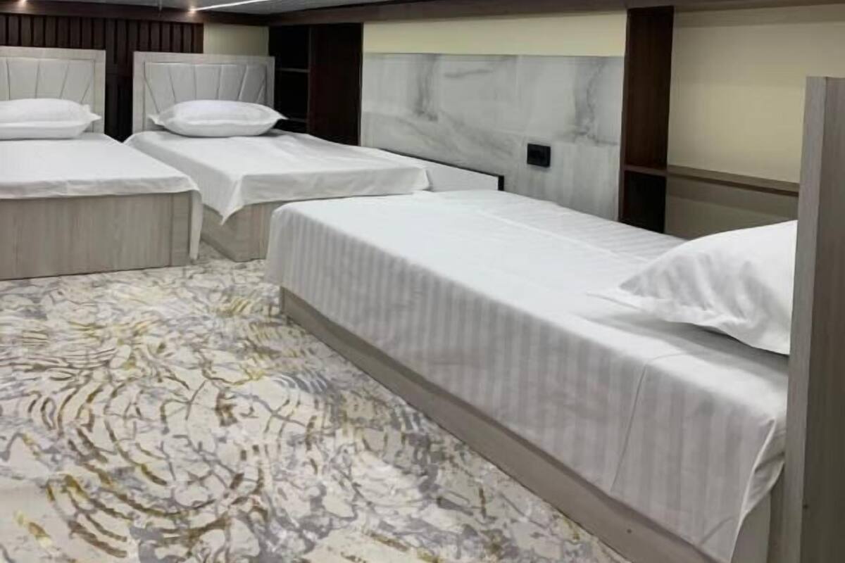 Habitación de hotel con tres camas, un cabecero de mármol y una alfombra estampada.