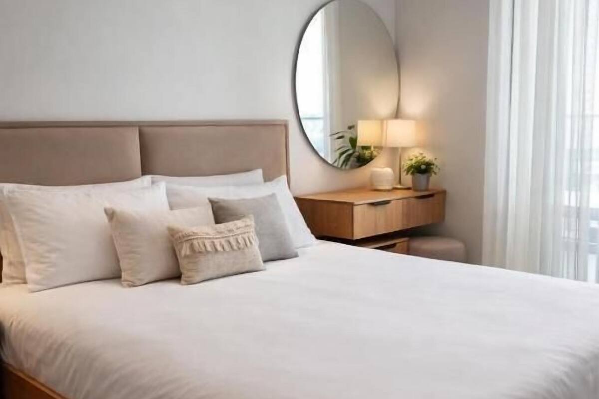 Un dormitorio con cama, mesita de noche, lámpara y espejo.