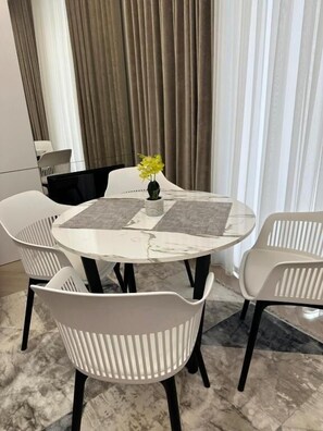 A round dining table with a marble top, surrounded by white chairs with black legs. - Nestone - Apartment Hotels (Tashkent)