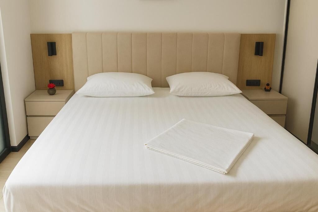 A neatly made bed with a beige headboard, two bedside tables with small decorative items, and a folded white towel on the bed.