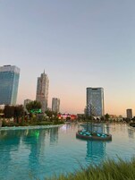 A cityscape with modern high-rise buildings, a central water feature, and a clear sky.