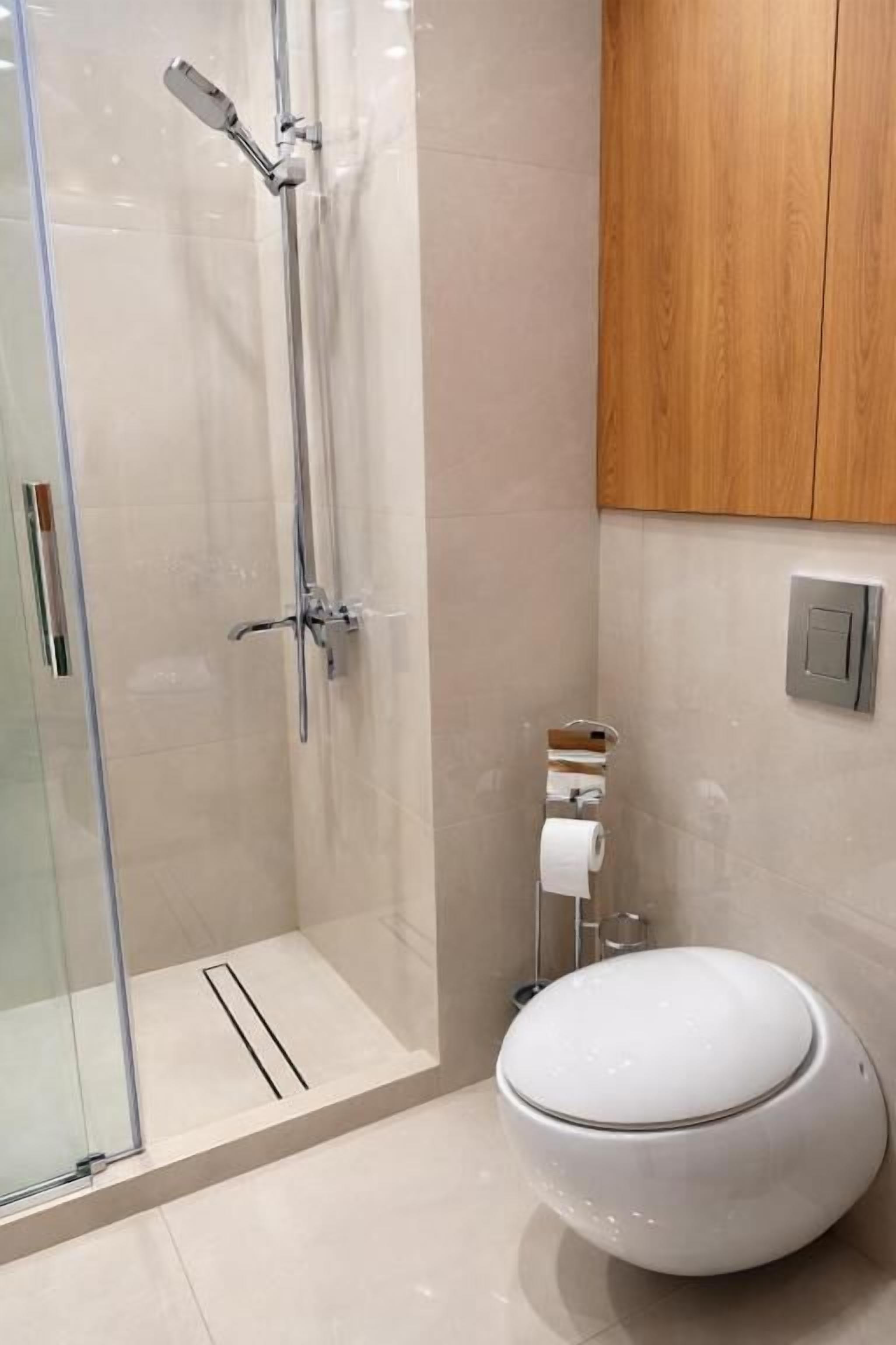 A bathroom with a glass shower enclosure, a toilet, and a wooden cabinet.