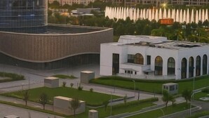 Moderni rakennuskompleksi, jossa on kaareva lasijulkisivu, valkoinen rakennus, jossa on holvikaari-ikkunat, sekä maisemoitu alue suihkulähteineen.