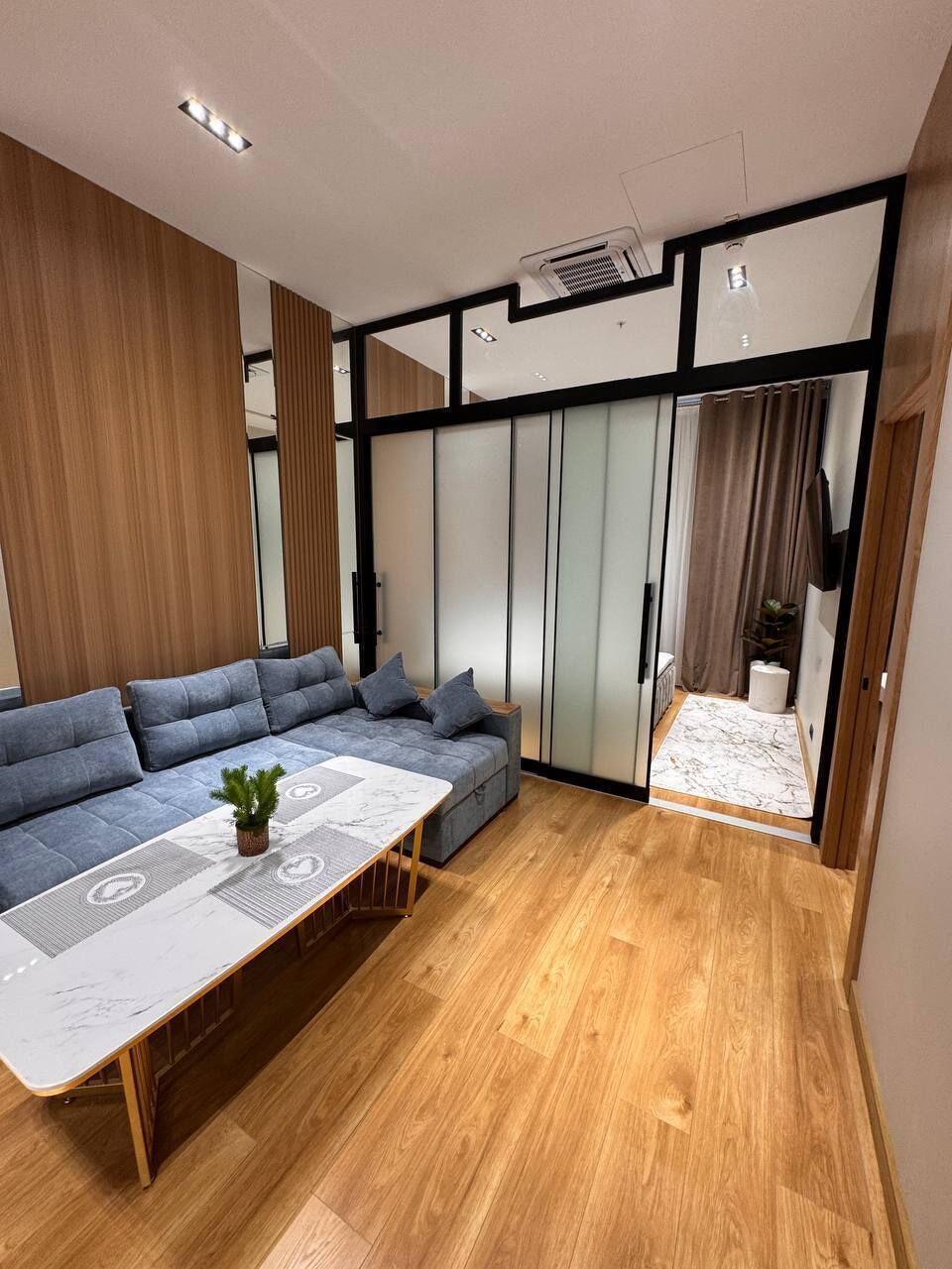 A modern living room with a sofa, a coffee table, and a sliding glass door leading to a balcony.