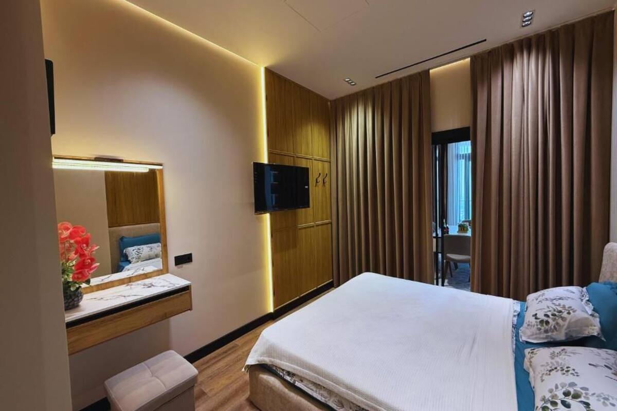 Una habitación de hotel moderna con una cama, un escritorio con espejo, un televisor y una ventana con cortinas.