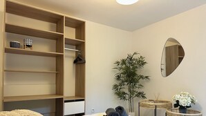 Ein Schlafzimmer mit einem Bett, einem großen Kleiderschrank, einem Spiegel, einem Blumentopf und einem kleinen Tisch mit einer Vase.