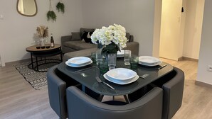 Ein Essbereich mit einem runden Tisch, gedeckt für vier Personen, umgeben von Stühlen, und eine Couch im Hintergrund.