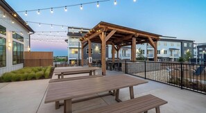 An outdoor patio with wooden benches and string lights. - Landing Amazing 1bd, Clubhouse, Gym (Kyle)