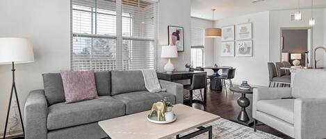 A modern living room with a grey sofa, a coffee table, and a dining area with a table and chairs.