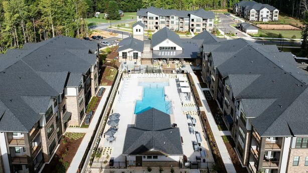 A modern apartment complex with a central swimming pool, multiple buildings, and a surrounding wooded area. - Landing Apartments Charlotte near Bradfield Farms (Charlotte)