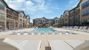 A pool area with lounge chairs, a pool, and multi-story buildings with balconies. - Landing Apartments Charlotte near Bradfield Farms (Charlotte)