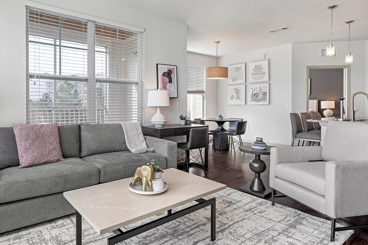 A modern living room with a grey sofa, a coffee table, and a dining area with a table and chairs.