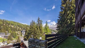 A mountain lodge with stone walls, a wooden fence, and a view of snow-capped mountains.