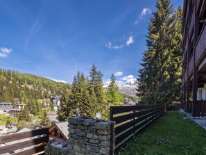 Eine Berghütte mit Steinmauern, einem Holzzaun und Blick auf schneebedeckte Berge.
