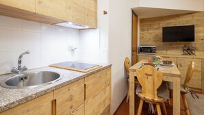 A kitchen with wooden cabinets, a granite countertop, a stainless steel sink, a microwave, and a dining area with wooden chairs.