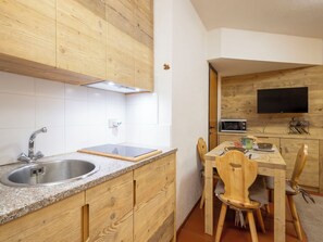 A kitchen with wooden cabinets, a granite countertop, a stainless steel sink, a microwave, and a dining area with wooden chairs.