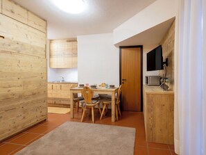 Eine kleine Küche mit Holzschränken, einem Esstisch mit Stühlen, einem kleinen Fernseher und einer Mikrowelle.