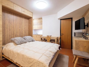 Ein Schlafzimmer mit einem Bett, einem Holztisch, einem Stuhl, einem Fernseher und einer Mikrowelle.