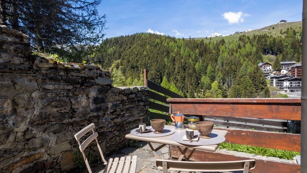 A stone wall, a wooden bench, a table with two bowls, a cup, and a coffee pot.