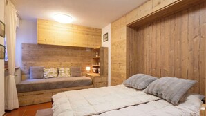 A bedroom with a bed, a sofa, a nightstand, and wooden paneling on the walls.
