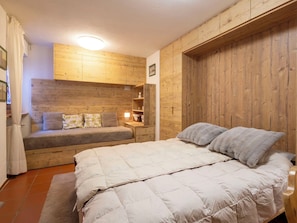 A bedroom with a bed, a sofa, a nightstand, and wooden paneling on the walls.