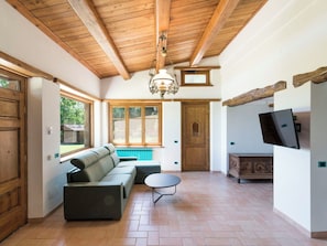Ein modernes Interieur mit Holzbalkendecke, einem Ecksofa, einem kleinen runden Tisch und einem Wand-Fernseher.