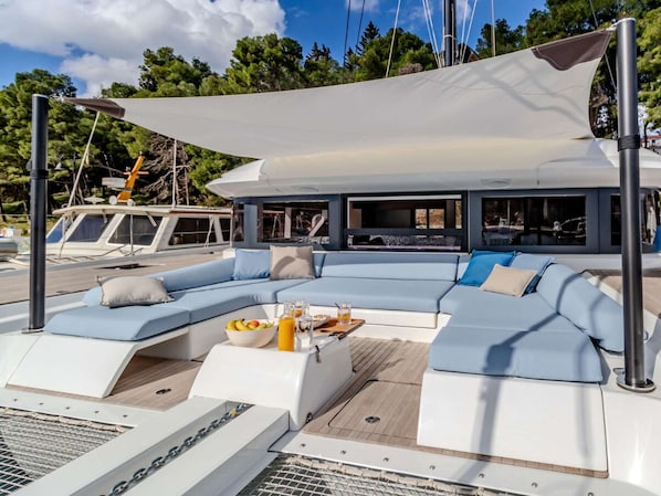 Un yacht dotĂ© dâun espace salon couvert, dâune table Ă manger avec des boissons, et offrant une vue sur le port de plaisance.