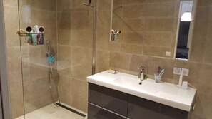 Une salle de bain moderne équipée d’une douche, d’un lavabo avec miroir et d’articles de toilette.
