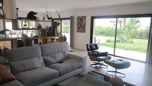 A modern living room with a sofa, a glass coffee table, and a dining area with a table and chairs. - Quiet, modern villa with swimming pool 5 minutes' walk from the village (Tourrettes-sur-Loup)
