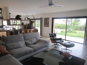 A modern living room with a sofa, a glass coffee table, and a dining area with a table and chairs. - Quiet, modern villa with swimming pool 5 minutes' walk from the village (Tourrettes-sur-Loup)