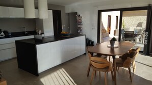 A modern kitchen with a central island, dining table with chairs, and a view to an outdoor area. - Quiet, modern villa with swimming pool 5 minutes' walk from the village (Tourrettes-sur-Loup)