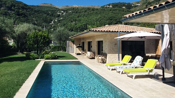 A rectangular swimming pool with clear water, surrounded by a paved deck. There are lounge chairs with cushions, a covered outdoor seating area, and a stone building with a tiled roof. - Quiet, modern villa with swimming pool 5 minutes' walk from the village (Tourrettes-sur-Loup)