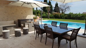 Une terrasse extérieure avec une piscine, des meubles en osier et un mur en pierre.