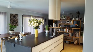A modern kitchen with a central island, a dining area with a table and chairs, and a bookshelf filled with books and decorative items. - Quiet, modern villa with swimming pool 5 minutes' walk from the village (Tourrettes-sur-Loup)
