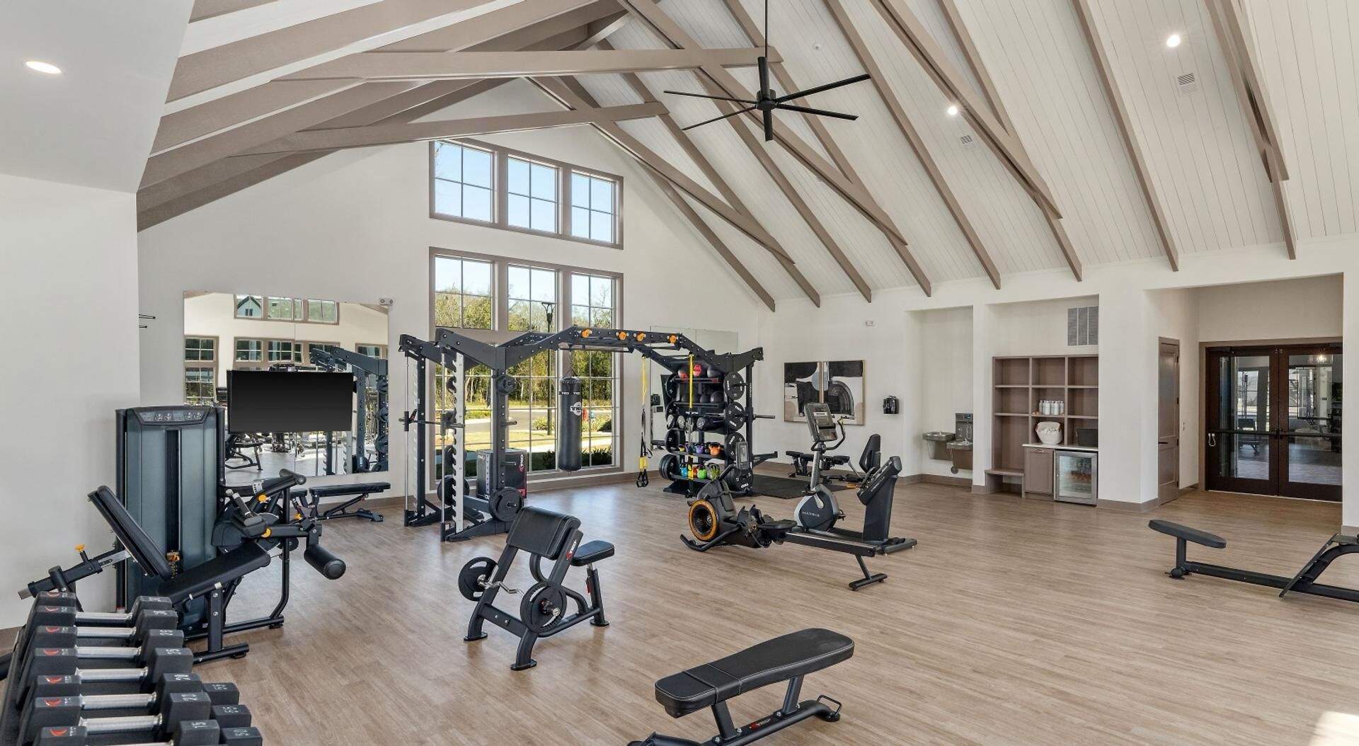 A spacious gym with various exercise equipment, large windows, and a high ceiling.