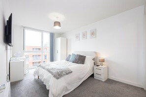 Una camera da letto moderna con un letto, un comodino, una lampada e un televisore montato a parete.