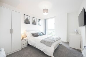 Ein modernes Schlafzimmer mit Bett, Nachttisch, Lampe, Kleiderschrank und Fernseher.
