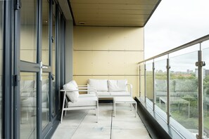 Un balcone con un divano bianco, un tavolino e una porta vetrata che dà su una stanza.
