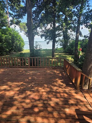 A wooden deck with a railing overlooking a grassy area and a body of water.