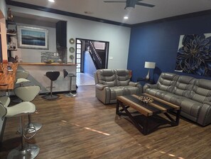 A modern living room with a leather sofa, a wooden coffee table, and a bar area with stools.