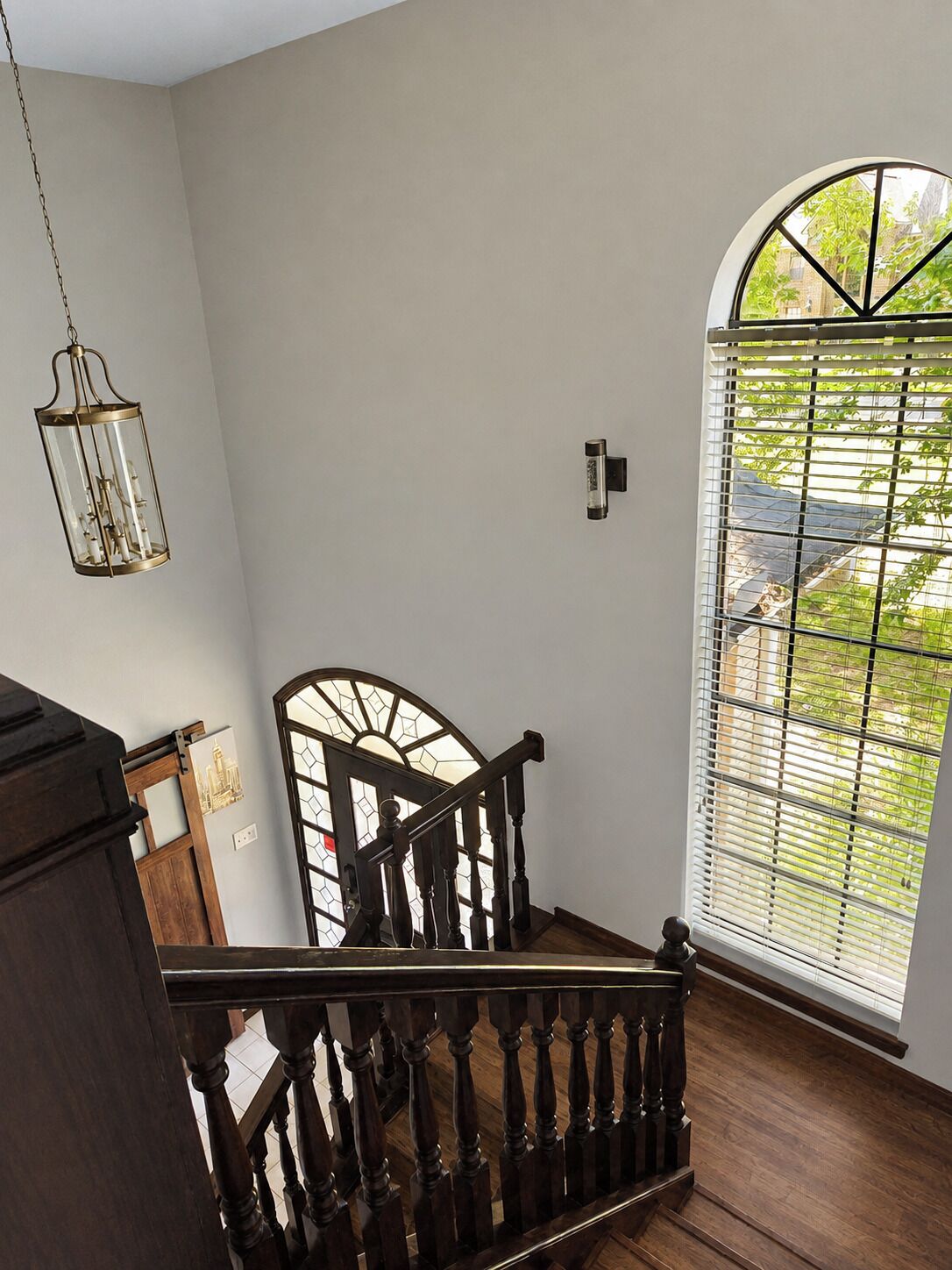A staircase with wooden balusters leading to a landing with a view through a window with a metal grid.
