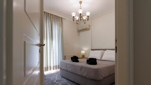 Ein Schlafzimmer mit einem Bett, einer Kandelaber, einer Klimaanlage, einem gemusterten Teppich und einem Fenster mit Vorhängen.