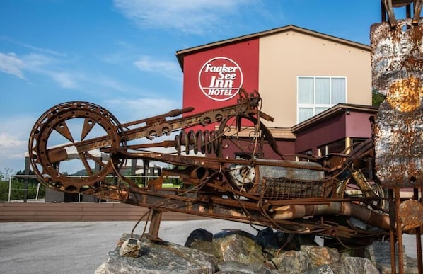 A large, rusted metal sculpture in front of a building with a red and beige facade and a sign that reads 'Fakker See Inn Hotel.' - Hotel Faaker See Inn by Aurora (Faak am See)