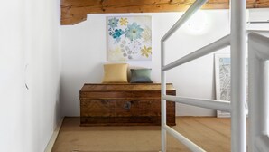 Eine Treppe führt zu einem Raum mit einer Holzkistenkommode, einem Kissen und einem floralen Gemälde an der Wand.