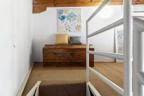 Eine Treppe führt zu einem Raum mit einer Holzkistenkommode, einem Kissen und einem floralen Gemälde an der Wand.