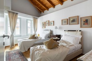 A bedroom with two beds, a window with curtains, a radiator, and framed pictures on the wall. - Nuccia Mansarda in heart of Como  (COMO)