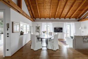 A spacious room with a wooden ceiling, a dining table with chairs, a television, and a sofa. - Nuccia Mansarda in heart of Como  (COMO)