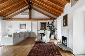 A spacious living area with a high wooden ceiling, a dining table with chairs, a sofa, a fireplace, and a large plant. - Nuccia Mansarda in heart of Como  (COMO)