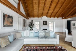 A spacious living room with a white sofa, wooden beams, and framed artwork. - Nuccia Mansarda in heart of Como  (COMO)